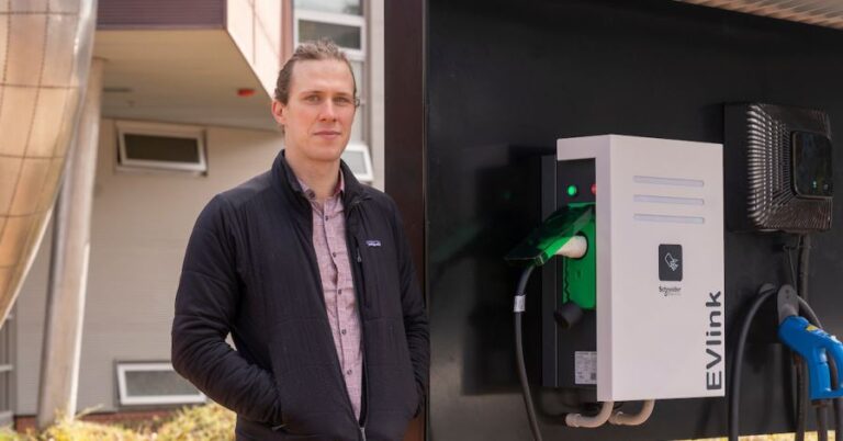 Bjorn Sturmberg standing next to electric vehicle chargers on campus