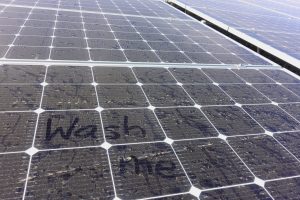 Solar panels wtih 'wash me' written in coating of dust